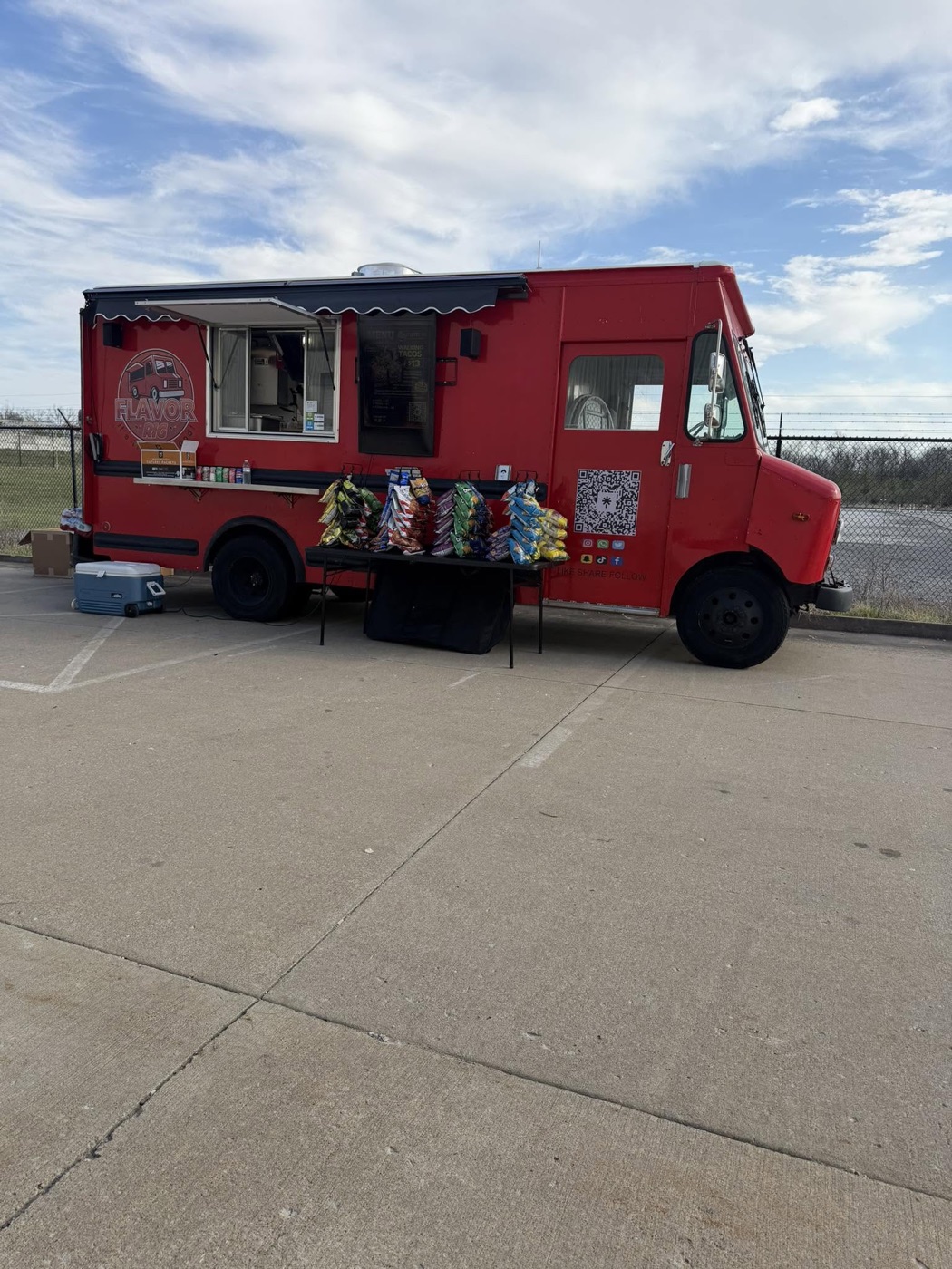 The red Flavor Rig food truck parked with its service window open and chip bags lined up on a table
