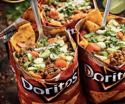 Two walking tacos served in open Doritos bags, loaded with seasoned meat, tomato, cucumber and sauce